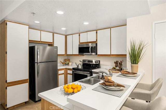 kitchen featuring sink, kitchen peninsula, white cabinets, and appliances with stainless steel finishes