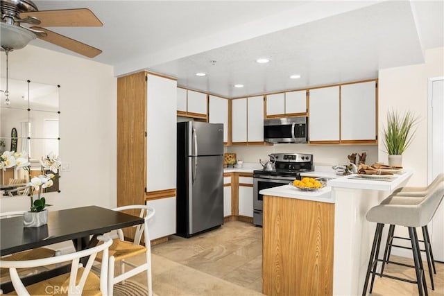 kitchen featuring appliances with stainless steel finishes, a breakfast bar, white cabinetry, ceiling fan, and kitchen peninsula