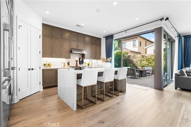 kitchen featuring tasteful backsplash, a kitchen bar, dark brown cabinetry, light hardwood / wood-style floors, and a center island with sink