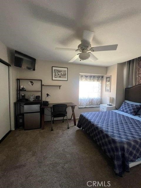 bedroom with ceiling fan, carpet floors, fridge, and a textured ceiling