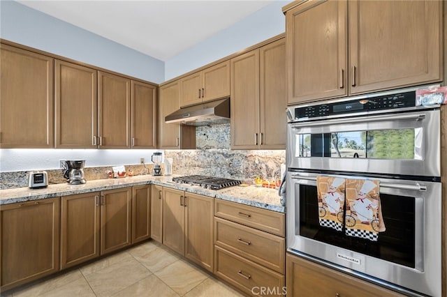 kitchen featuring appliances with stainless steel finishes, backsplash, under cabinet range hood, and light stone countertops