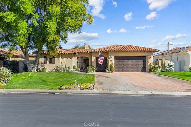 mediterranean / spanish-style house with a garage, fence, decorative driveway, stucco siding, and a front yard