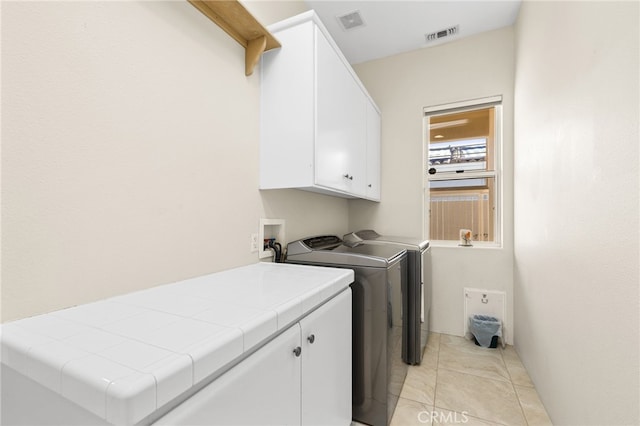 laundry area with visible vents, light tile patterned floors, washing machine and dryer, and cabinet space