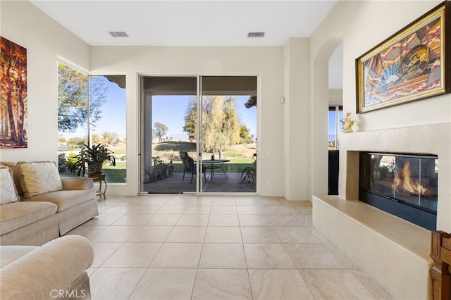 living room featuring light tile patterned floors, visible vents, arched walkways, and a glass covered fireplace