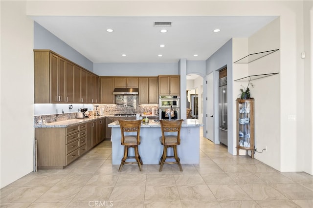 kitchen featuring arched walkways, visible vents, appliances with stainless steel finishes, a kitchen island, and under cabinet range hood