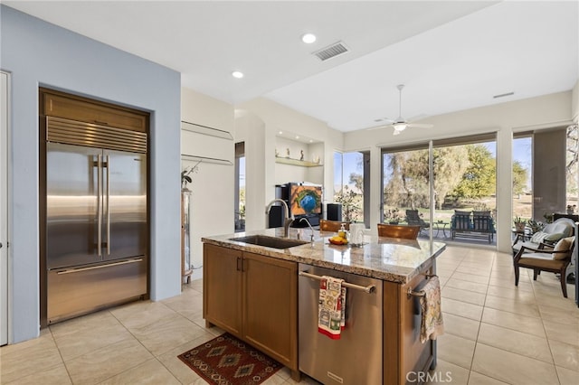 kitchen featuring stainless steel appliances, a sink, open floor plan, light stone countertops, and a center island with sink