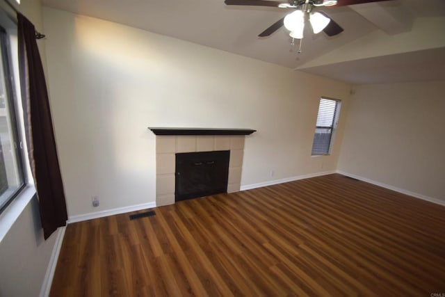 unfurnished living room with dark wood-type flooring, ceiling fan, a tiled fireplace, and vaulted ceiling with beams