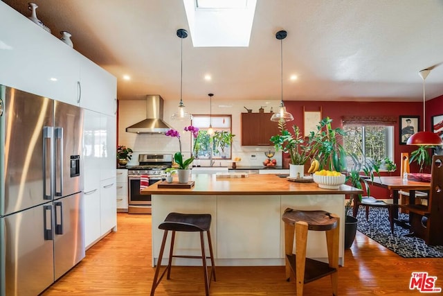 kitchen featuring appliances with stainless steel finishes, pendant lighting, a breakfast bar area, a center island, and wall chimney exhaust hood