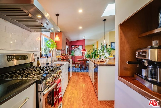 kitchen with lofted ceiling, decorative light fixtures, stainless steel range with gas cooktop, and ventilation hood