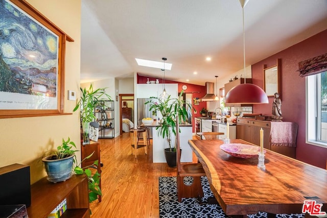 dining room with vaulted ceiling with skylight and light wood-type flooring