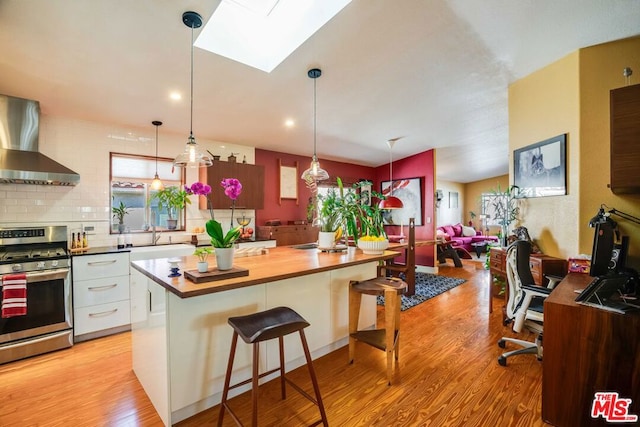 kitchen with a breakfast bar, gas range, white cabinetry, light wood-type flooring, and wall chimney range hood