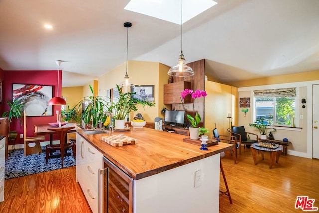 kitchen with wood counters, lofted ceiling with skylight, hanging light fixtures, light wood-type flooring, and beverage cooler