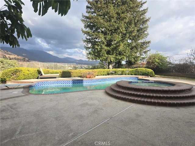 view of swimming pool with a mountain view, a patio area, and an in ground hot tub