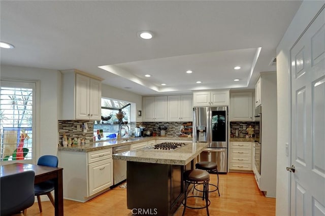 kitchen featuring a kitchen island, appliances with stainless steel finishes, a breakfast bar area, white cabinets, and a tray ceiling