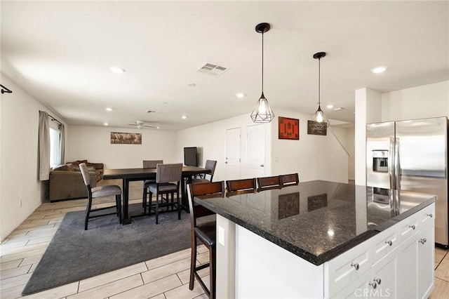 kitchen with dark stone countertops, stainless steel fridge, a kitchen island, pendant lighting, and white cabinets