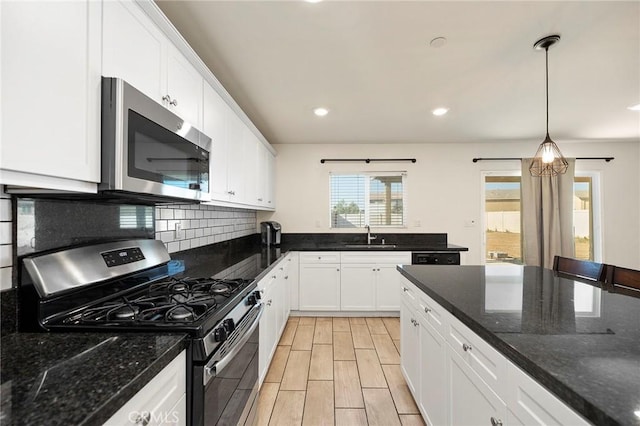 kitchen with pendant lighting, dark stone countertops, white cabinets, backsplash, and stainless steel appliances