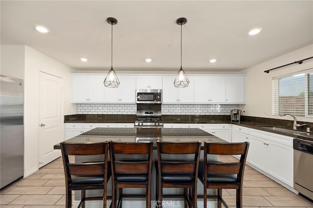 kitchen with sink, hanging light fixtures, appliances with stainless steel finishes, a kitchen island, and white cabinets