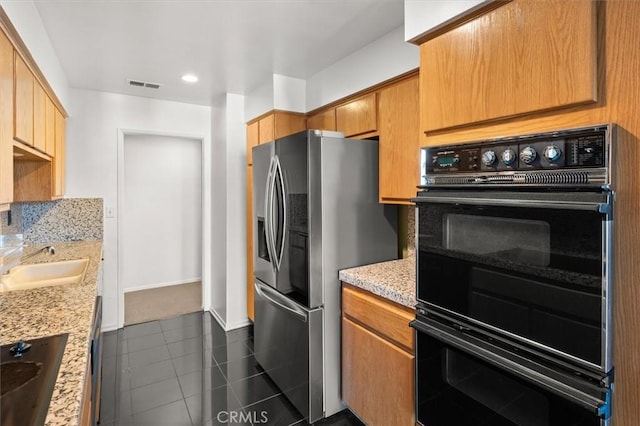 kitchen with double oven, sink, stainless steel fridge with ice dispenser, and light stone counters