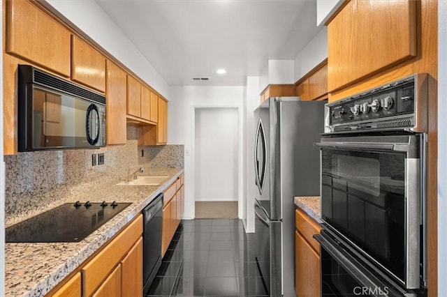 kitchen featuring sink, tasteful backsplash, light stone counters, black appliances, and dark tile patterned flooring