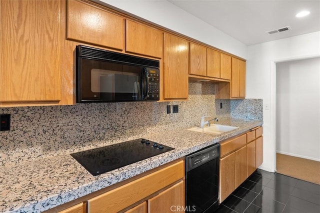 kitchen with sink, tasteful backsplash, light stone counters, black appliances, and dark tile patterned flooring