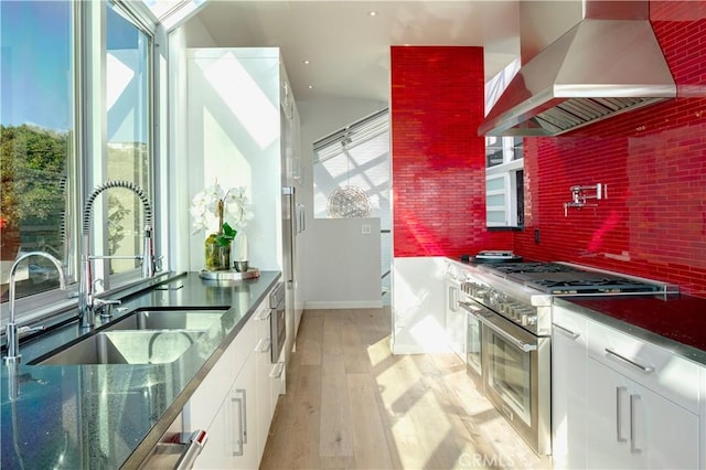 kitchen featuring sink, white cabinetry, high end range, light wood-type flooring, and range hood