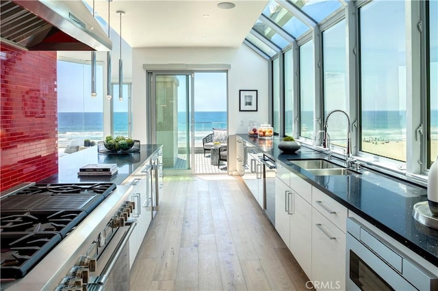 kitchen with extractor fan, white cabinetry, sink, hanging light fixtures, and a water view