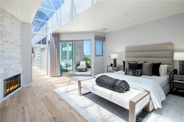 bedroom featuring a large fireplace, a wall mounted air conditioner, access to exterior, and light hardwood / wood-style floors