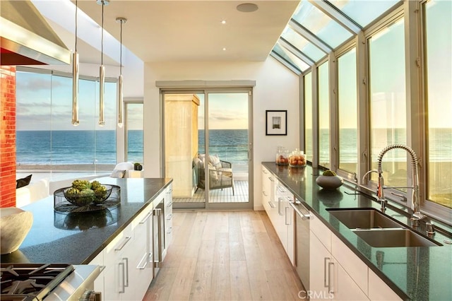 kitchen with pendant lighting, sink, white cabinetry, dark stone countertops, and a water view