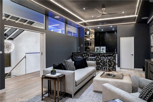 living room featuring a raised ceiling, ceiling fan, and light hardwood / wood-style floors