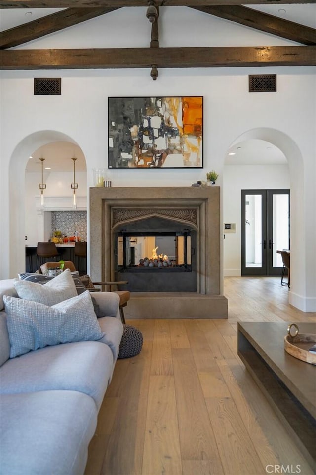 living room featuring light wood-type flooring, lofted ceiling with beams, french doors, and a multi sided fireplace