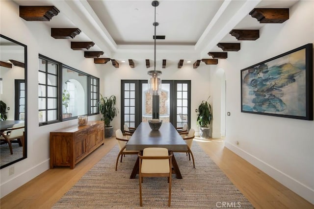 dining room featuring french doors, a raised ceiling, and light wood-type flooring