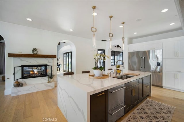 kitchen featuring pendant lighting, sink, light stone counters, high quality fridge, and an island with sink