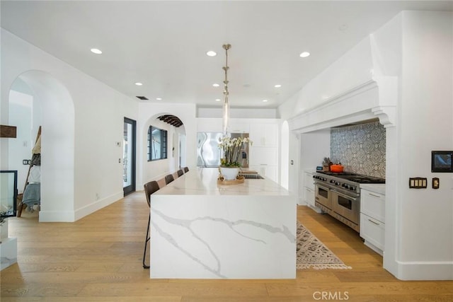 kitchen with pendant lighting, appliances with stainless steel finishes, white cabinetry, light stone countertops, and a kitchen island