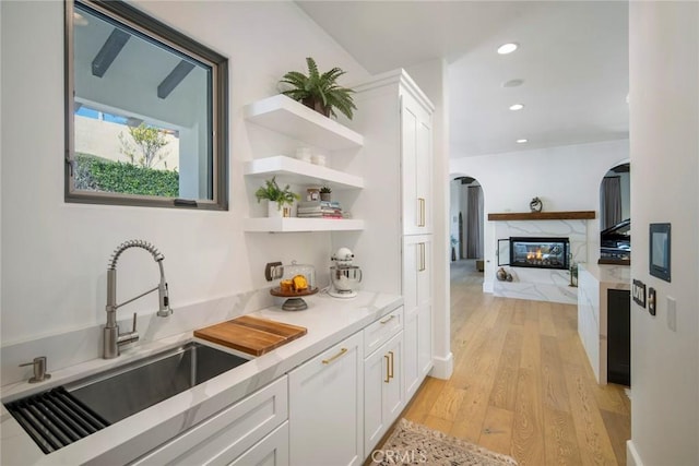 bar featuring a premium fireplace, white cabinetry, sink, and light hardwood / wood-style flooring