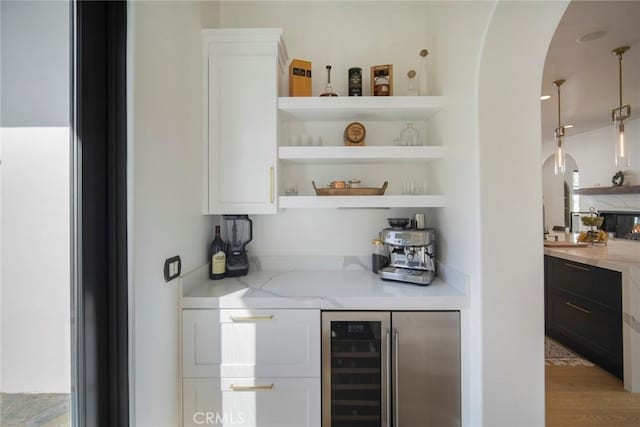 bar featuring wine cooler, light stone counters, light hardwood / wood-style floors, and white cabinets