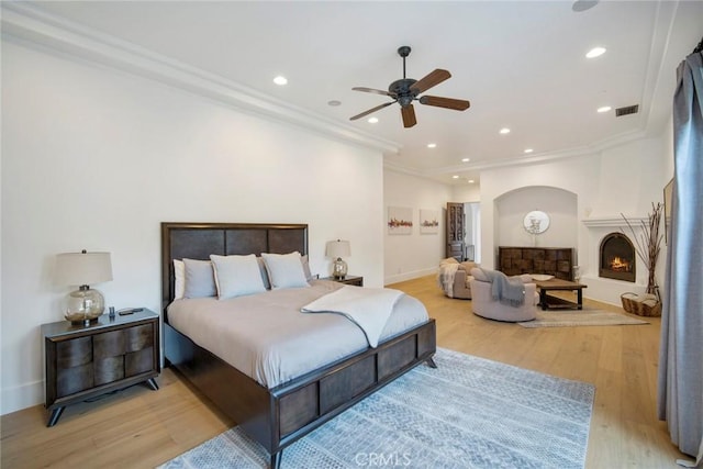 bedroom featuring a large fireplace, ornamental molding, and light hardwood / wood-style flooring