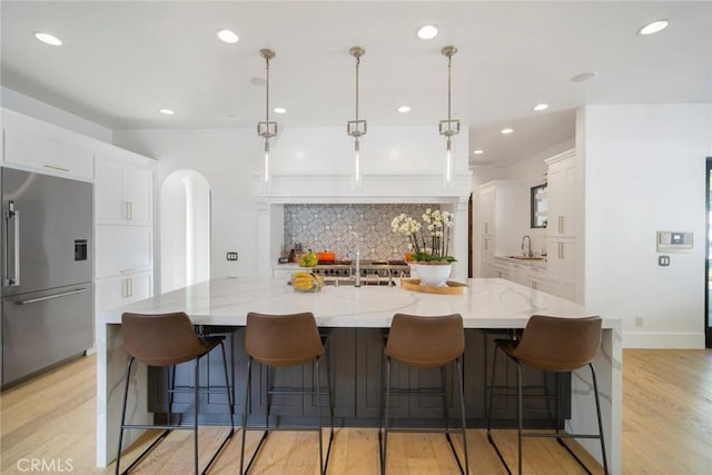 kitchen featuring a spacious island, built in fridge, light stone counters, and pendant lighting