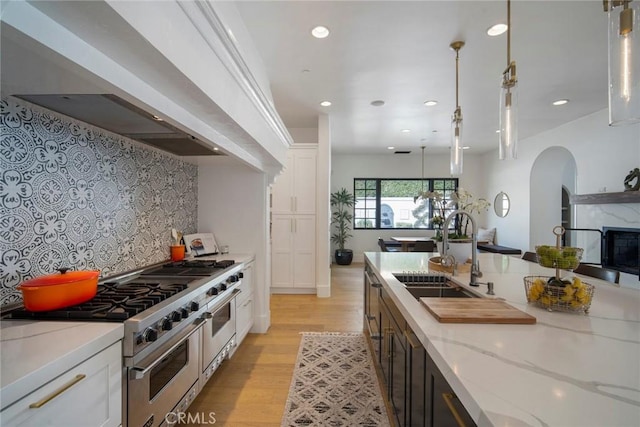 kitchen with pendant lighting, sink, white cabinetry, light stone countertops, and range with two ovens