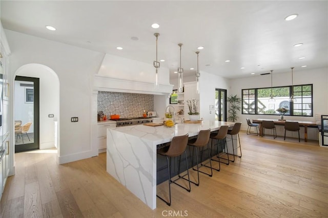 kitchen featuring a spacious island, white cabinetry, pendant lighting, light stone countertops, and light hardwood / wood-style floors