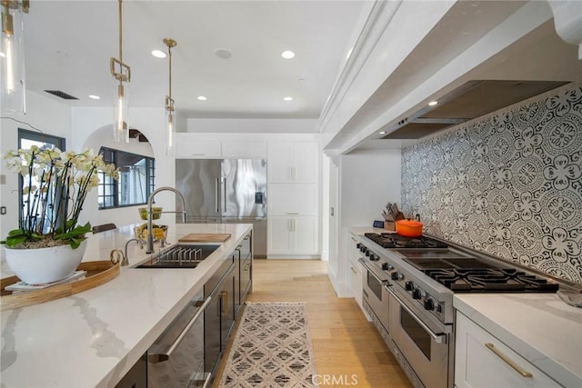 kitchen with sink, custom exhaust hood, light stone counters, white cabinetry, and stainless steel appliances