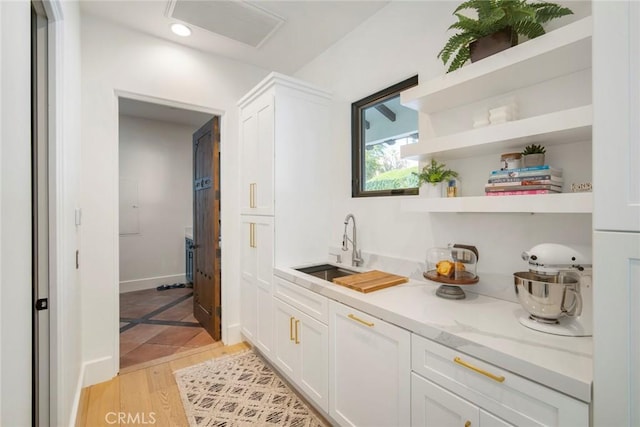 bar featuring white cabinetry, sink, light stone counters, and light hardwood / wood-style flooring