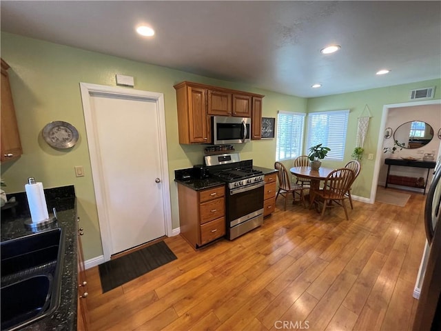 kitchen featuring dark stone countertops, sink, light hardwood / wood-style flooring, and stainless steel appliances