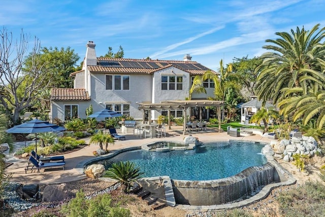 rear view of property with a swimming pool with hot tub, a pergola, a patio, and solar panels