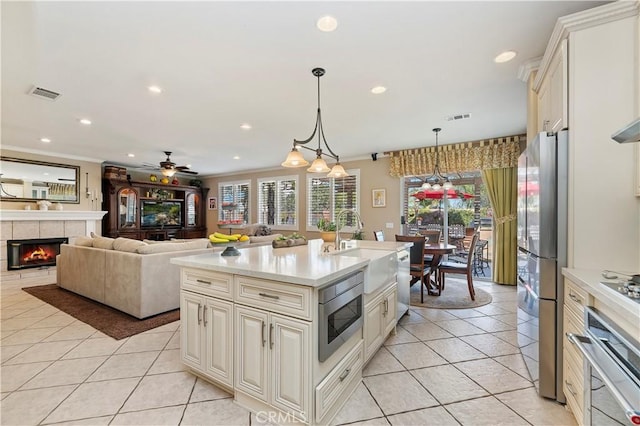 kitchen with a fireplace, decorative light fixtures, sink, a kitchen island with sink, and stainless steel appliances