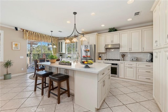 kitchen with pendant lighting, light tile patterned floors, a breakfast bar area, appliances with stainless steel finishes, and a kitchen island with sink