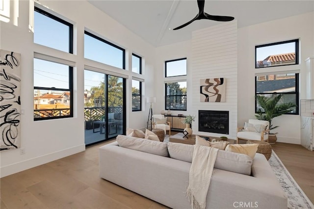 living room featuring ceiling fan, a towering ceiling, a fireplace, and light hardwood / wood-style floors