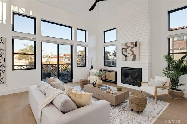 living room featuring a high ceiling, a healthy amount of sunlight, a fireplace, and light hardwood / wood-style flooring