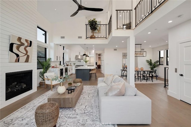 living room featuring ceiling fan, a fireplace, light hardwood / wood-style flooring, and a high ceiling