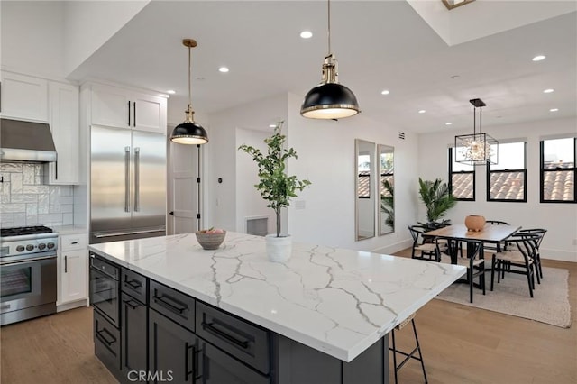 kitchen with a center island, hanging light fixtures, high quality appliances, light stone countertops, and white cabinets