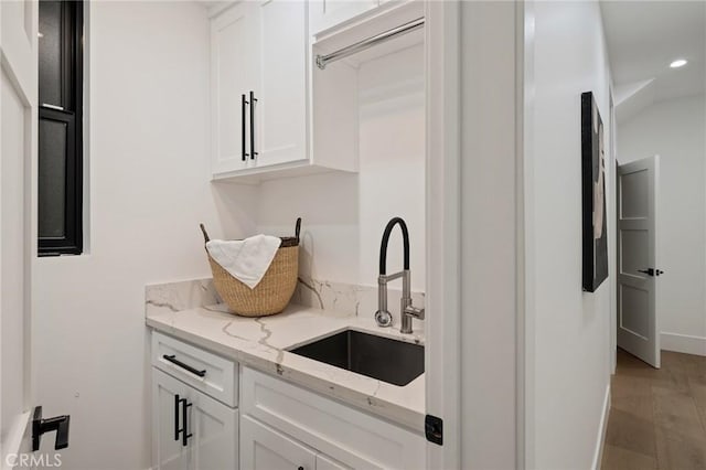 kitchen with light stone countertops, sink, white cabinets, and light hardwood / wood-style floors